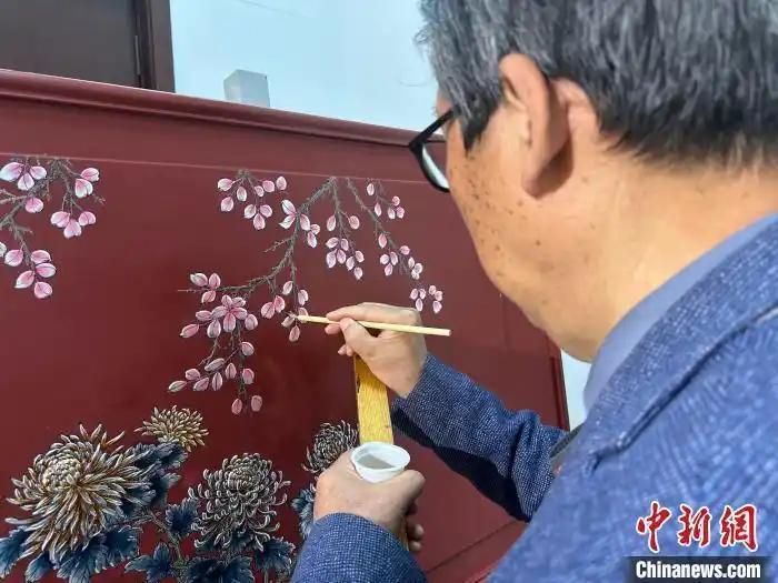 梁中秀拿着画笔,认真地揣摩着一幅漆画的制作。刘小红 摄